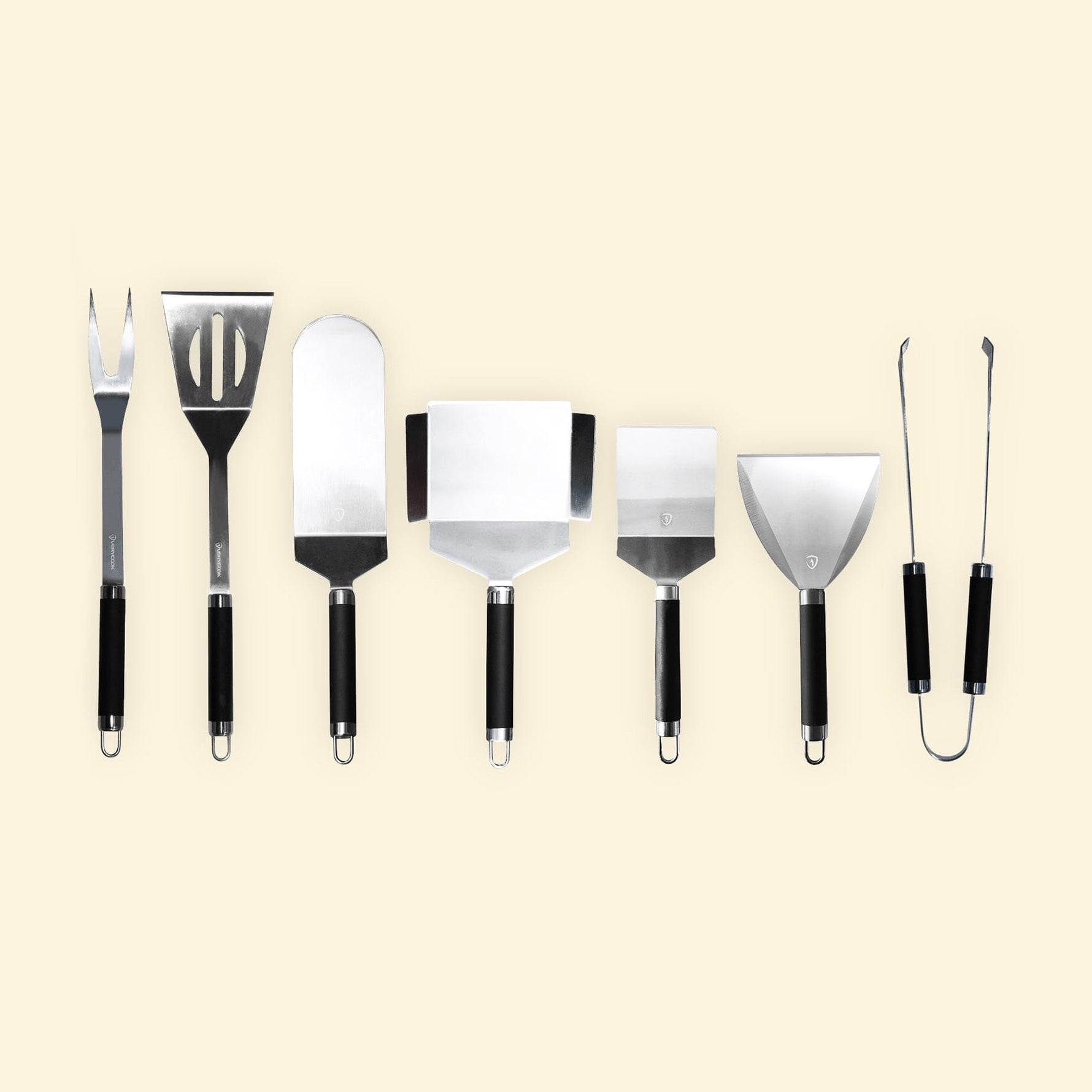 Lot de 7 ustensiles de cuisine en inox avec manches noirs alignés sur fond beige, comprenant, fourchette, spatules, racloirs et pince.