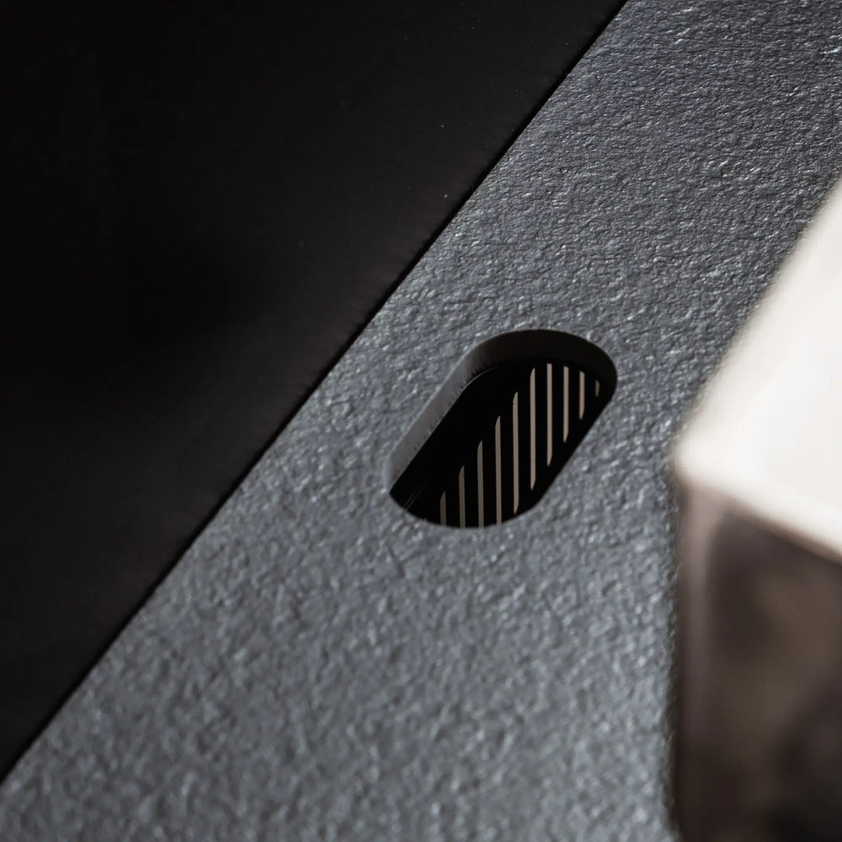 Detail der integrierten Kabeldurchführung in der schwarzen Keramik-Arbeitsplatte Pilotis.\n::visuel:noir