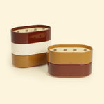 Bougies Totem L Rouge oxyde – Citronnelle & Géranium et Brun terre de sienne – Citronnelle & Fleur d’oranger, deux grandes bougies ovales à triple mèche en bois, posées sur un fond beige clair.