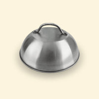 Cloche de cuisson en inox posée sur fond uni, accessoire pour plancha permettant de créer un effet four et de maintenir la chaleur.