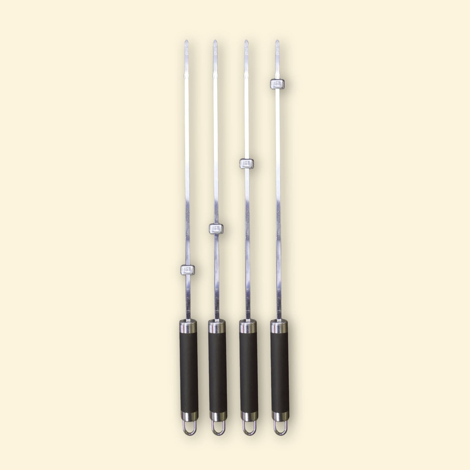 Lot de quatre brochettes longues en inox avec manche noir et bagues réglables, alignées sur fond beige.