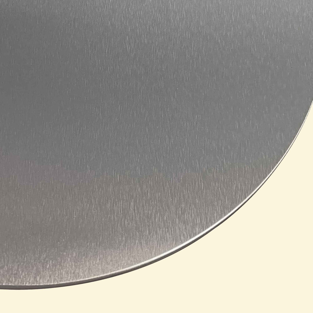 Gros plan sur la surface brossée en inox d’une grande pelle à pizza, montrant le bord arrondi et la finition métallique.