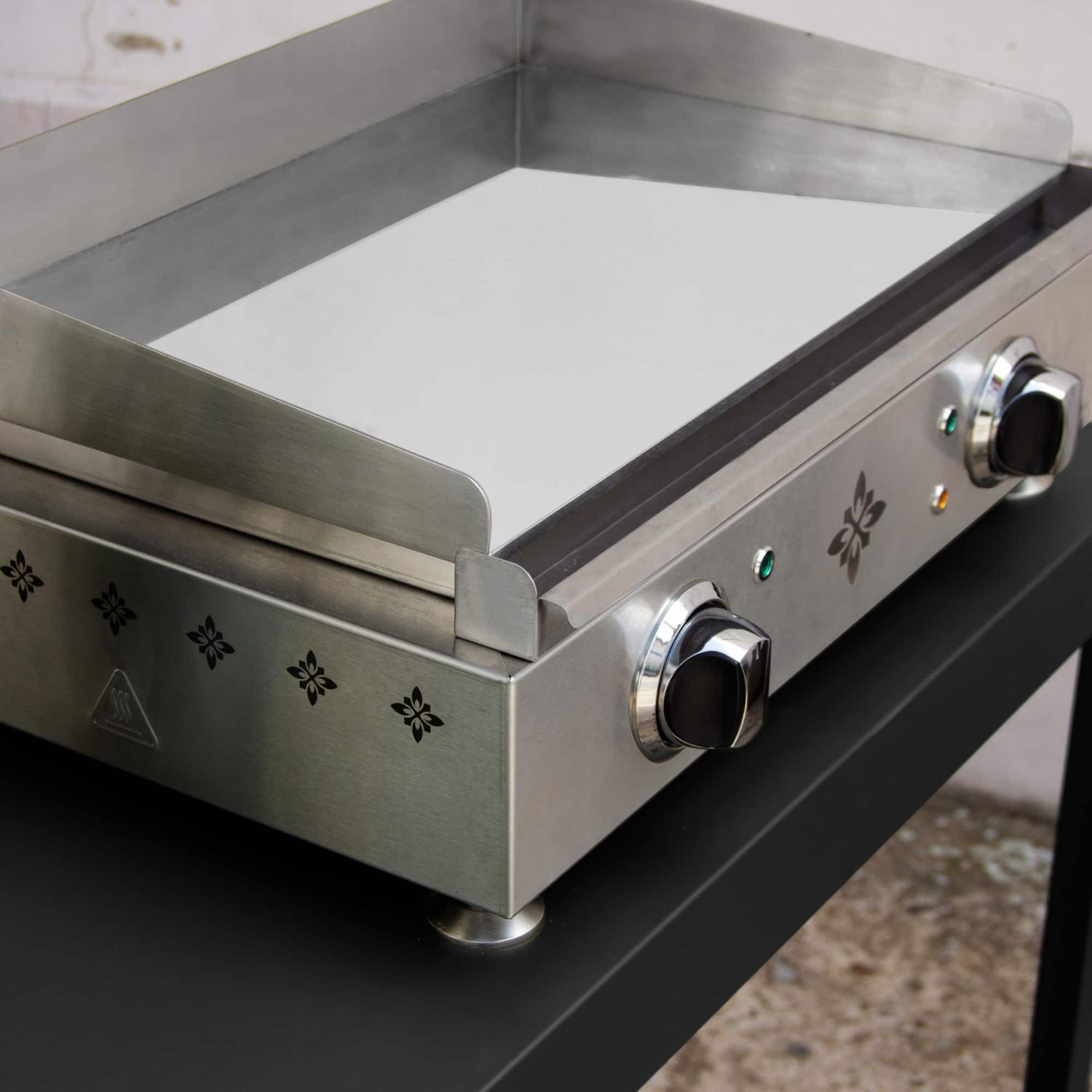 Vue rapprochée de la plancha électrique Vivaplancha avec sa plaque en chrome dur brillante, entourée de rebords en inox et équipée de deux boutons de réglage sur la façade.